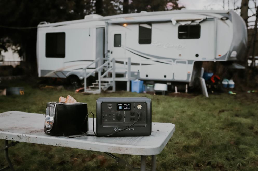 Camper using a laptop beside a portable power station at a nighttime campsite