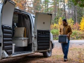 Camper carrying a portable power station beside a van among autumn trees