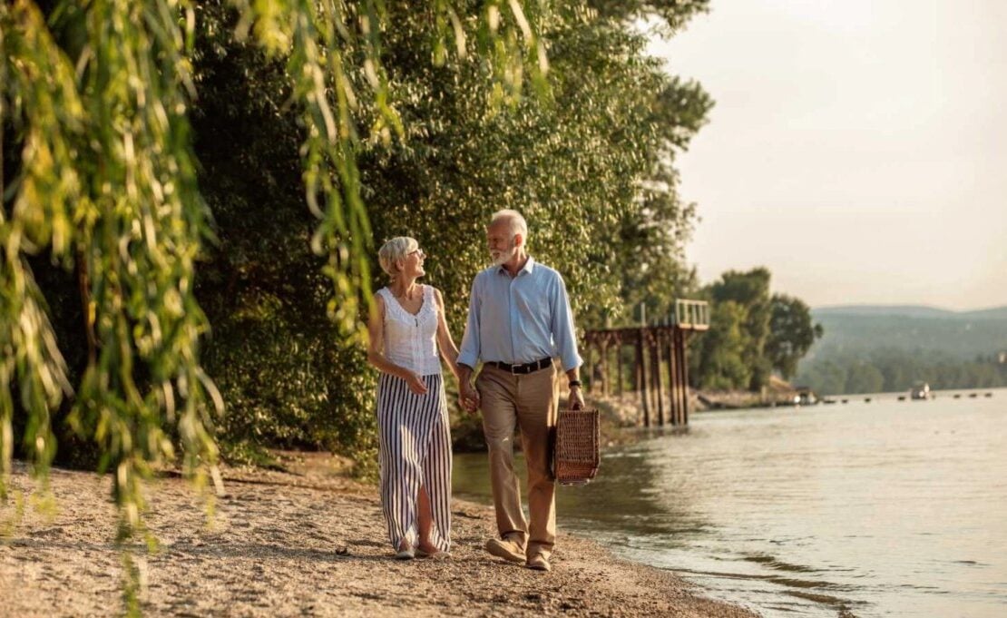 Mature couple walking beside a river with a picnic basket