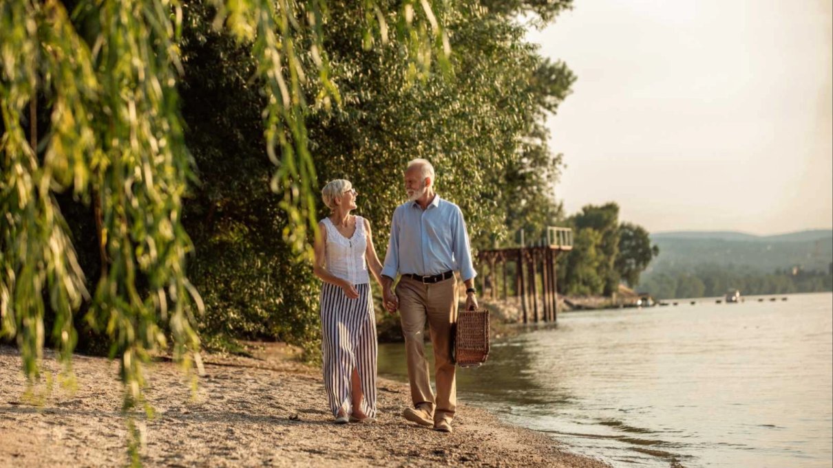 Mature couple walking beside a river with a picnic basket
