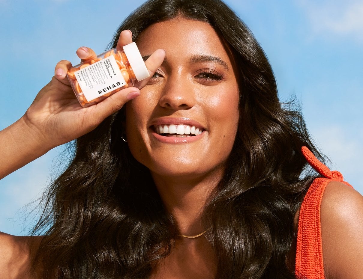 A person holding REHAB Dose 1.0 hair oil capsules