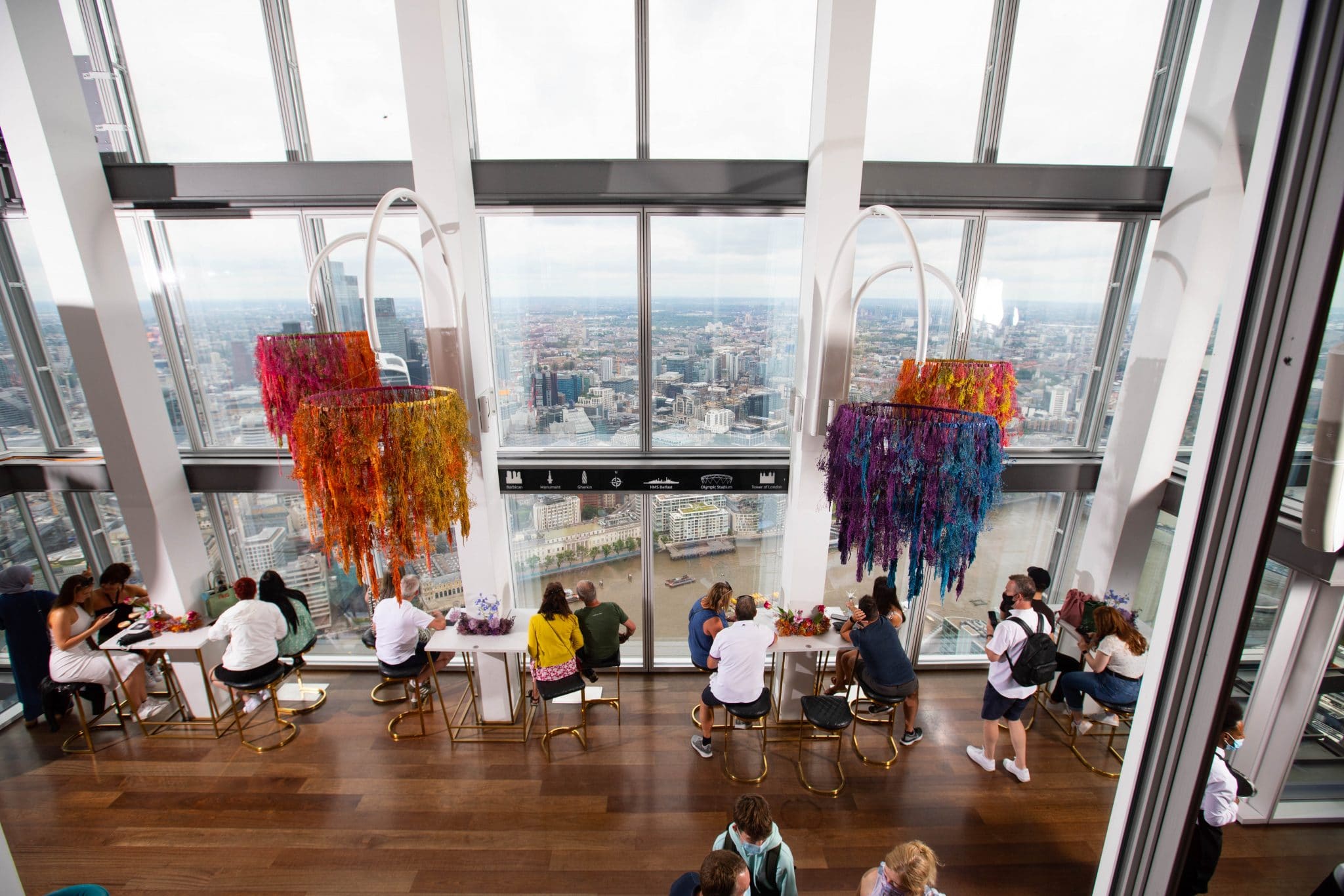 Visitors seated beside colourful art installations and windows overlooking London